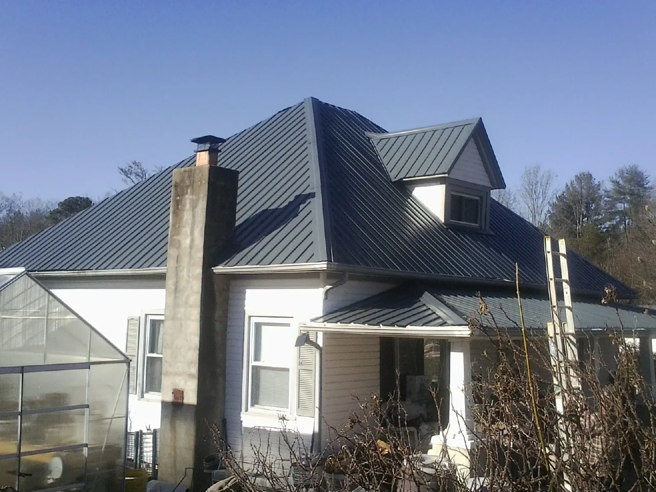 Dark blue standing seam metal roof on a white farmhouse with dormer — Slate & Tile Roof Repair by Roofing Brothers in Schoolcraft