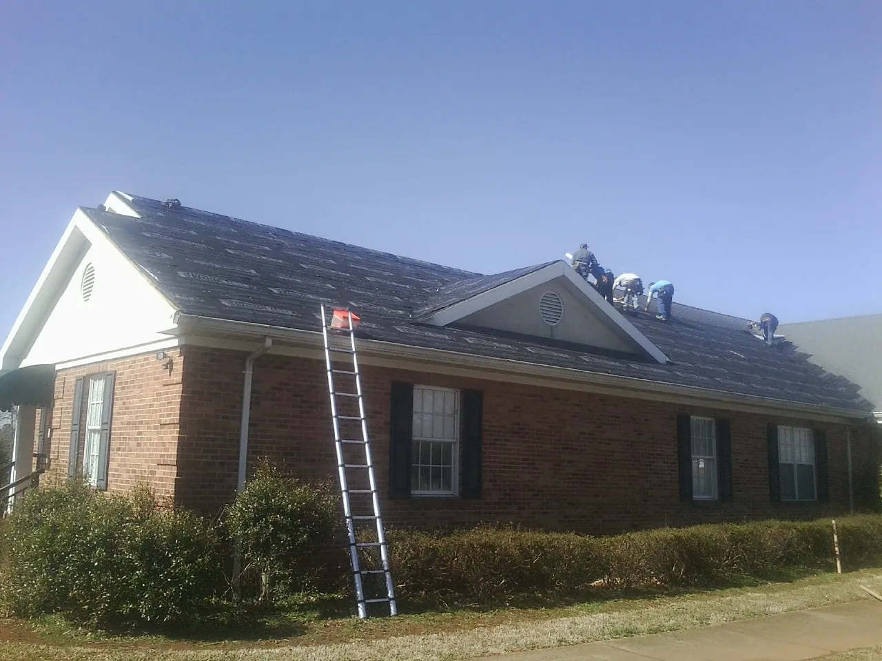 Crew tearing shingles off a brick ranch roof with a ladder set — Emergency Roof Repair work by our crew in Schoolcraft
