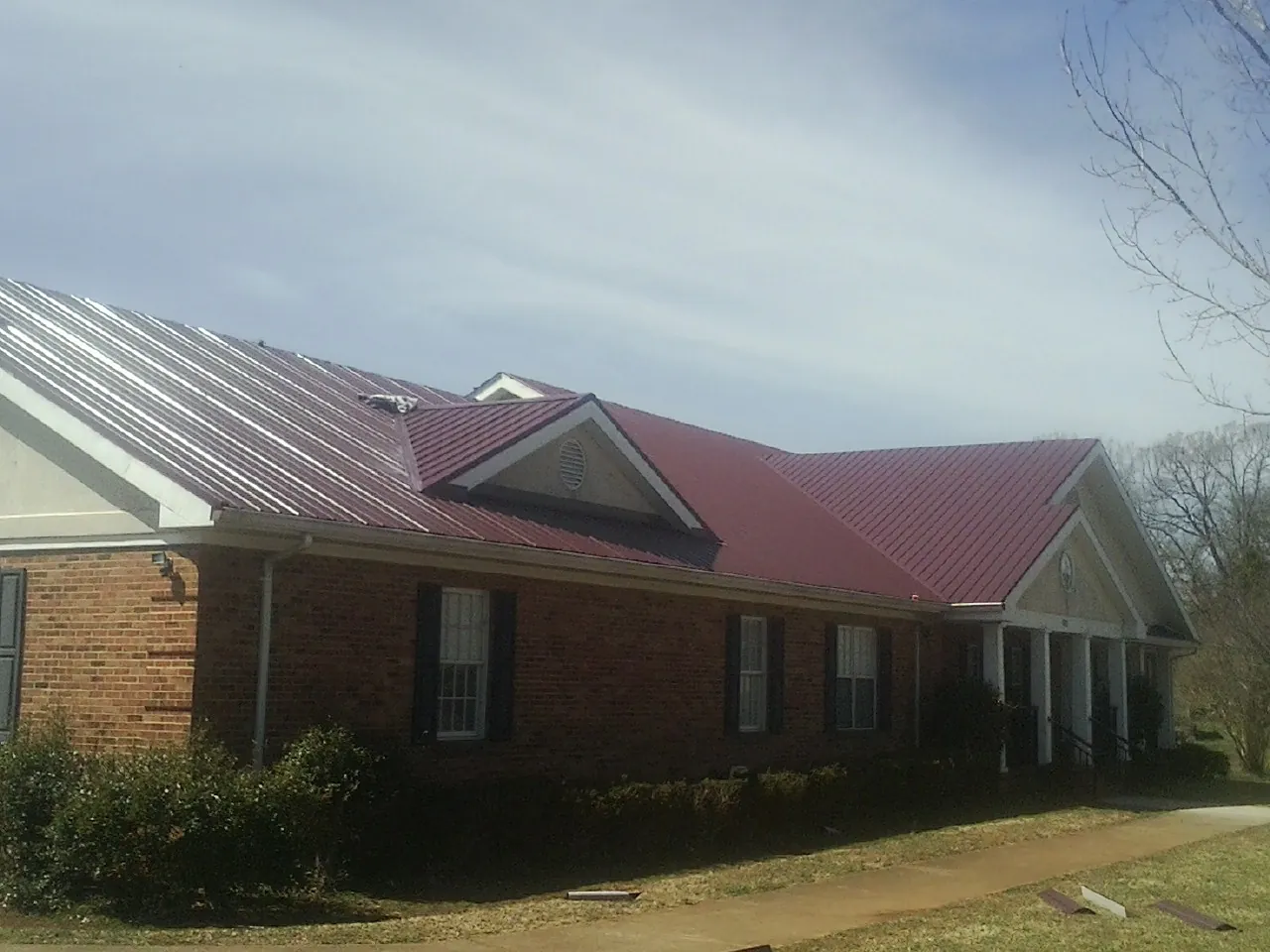 Red metal roof with gabled entries on a long brick building, from a Hail Damage Roof Repair job in Schoolcraft