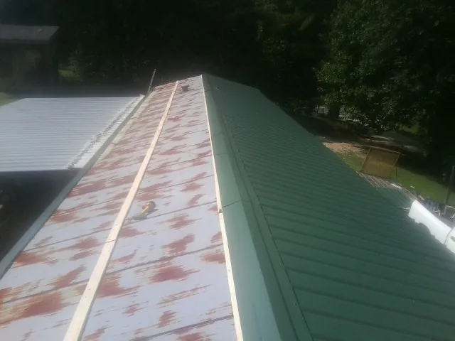 Old rusted panels beside newly installed green metal roofing — Wind Damage Roof Repair by Roofing Brothers in Schoolcraft