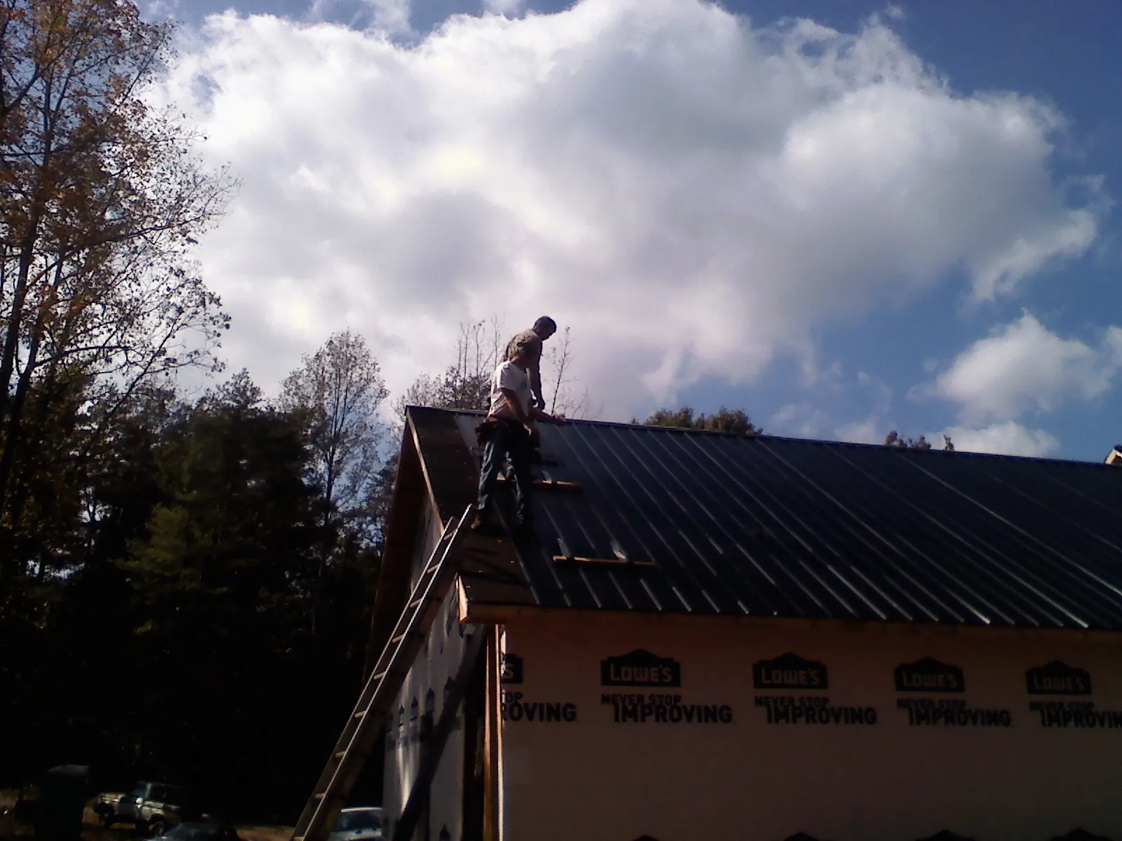 Roofer fastening dark metal panels high against a cloudy sky, from a Roof Inspection job in Schoolcraft