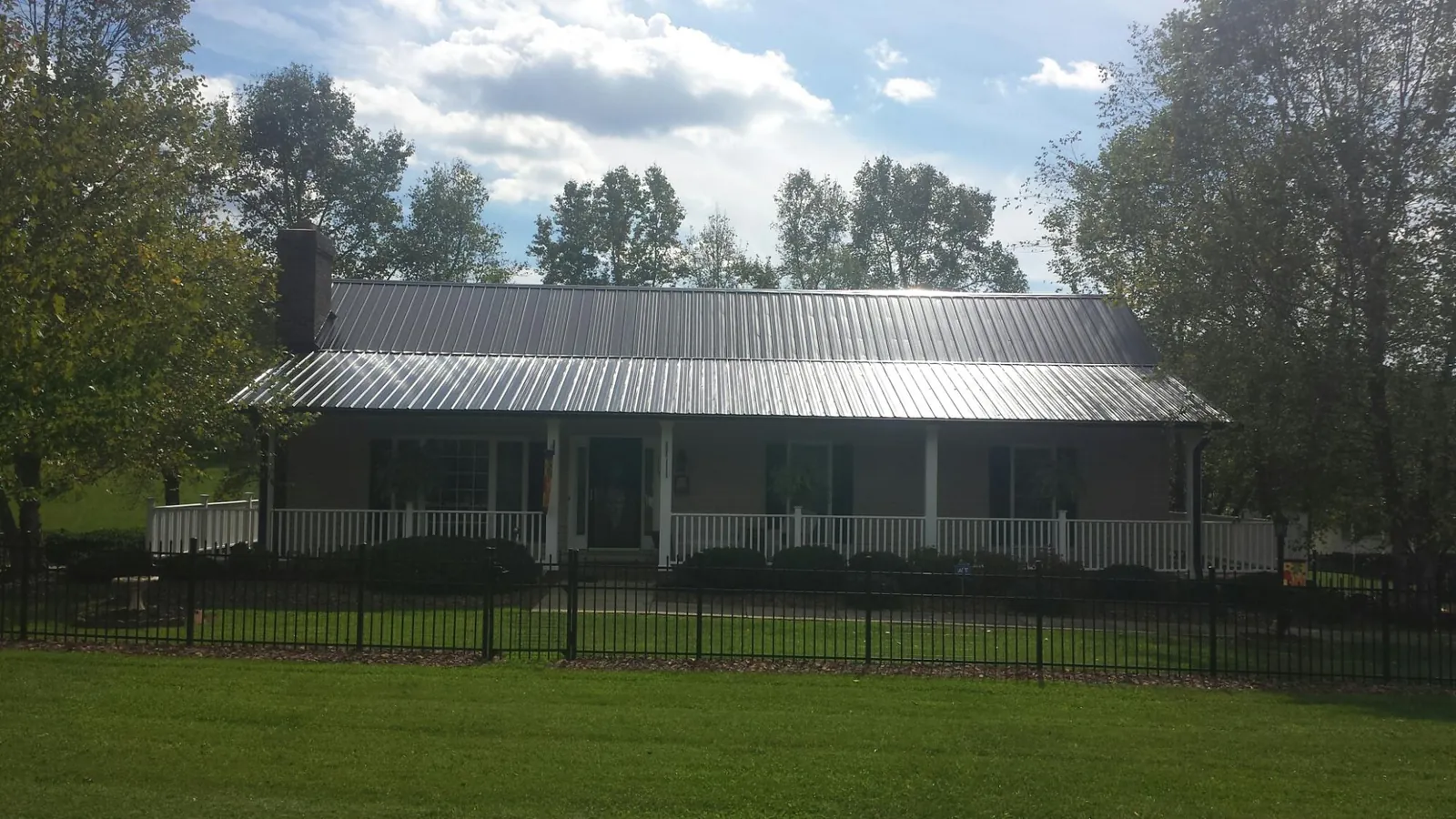 Gray metal roof on a brick ranch with a full width front porch — Gutter Guard Installation work by our crew in Schoolcraft