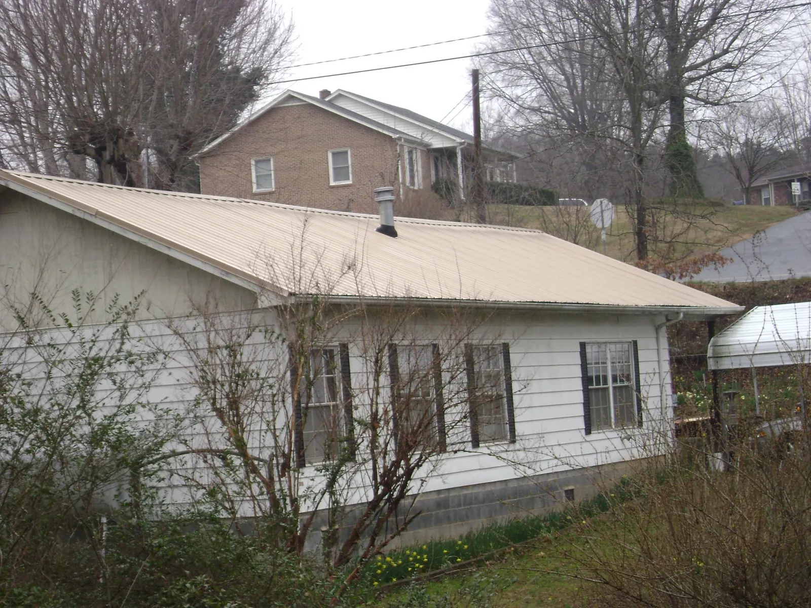 Tan metal roof on a white sided house set into a hillside — Commercial Roofing by Roofing Brothers in Schoolcraft