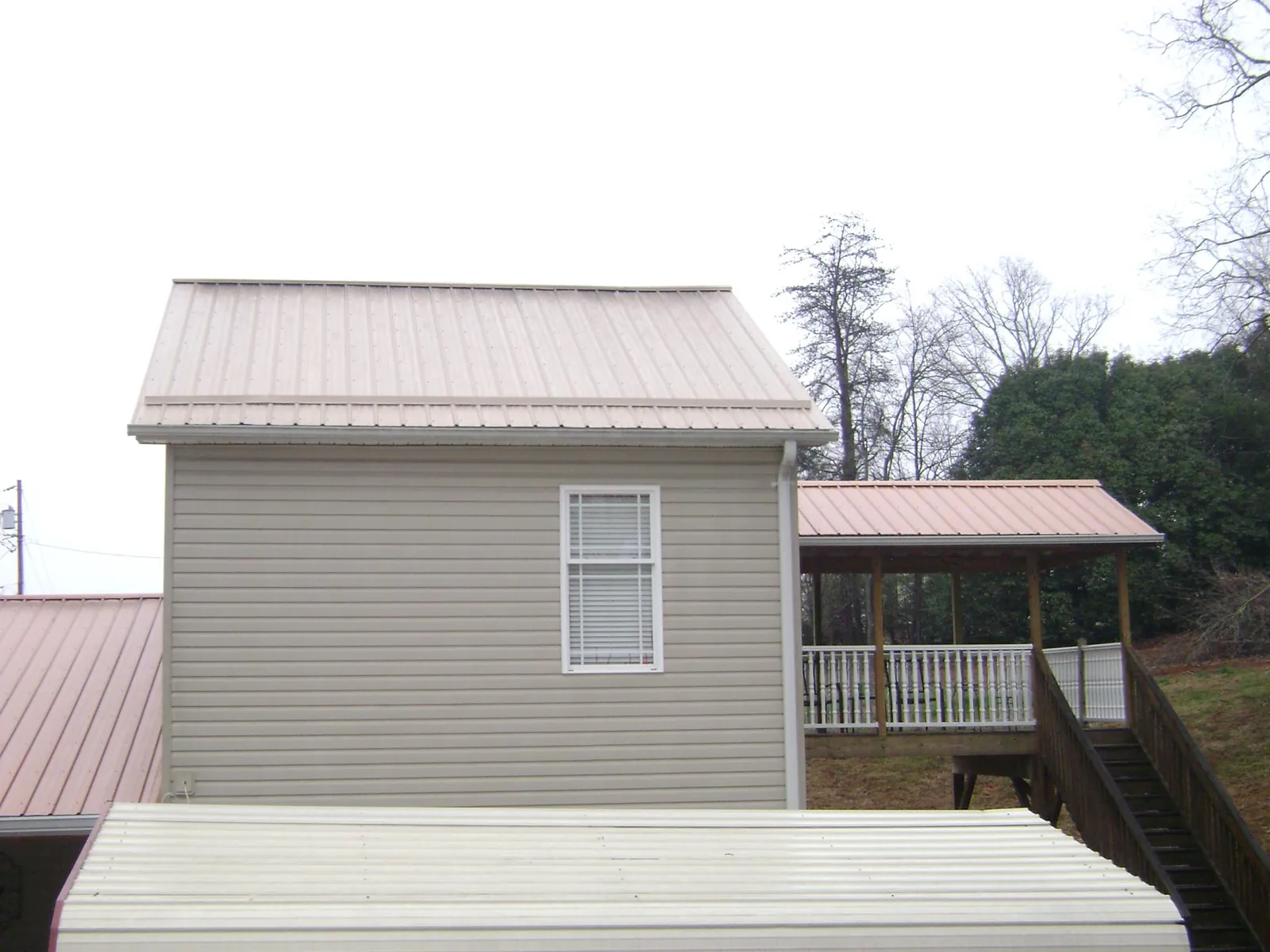 Tan metal roofs on a two story addition and attached porch, from a Roof Replacement job in Schoolcraft